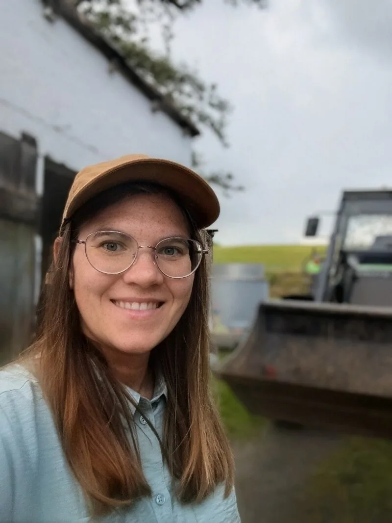 Theresa Bäuml mit Basecap und Brille auf einem Hof mit Traktor